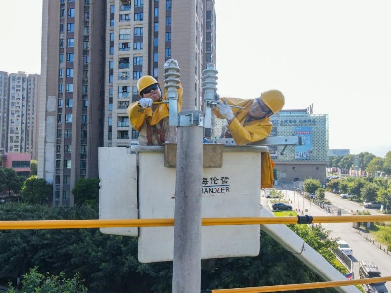 8月14日，在南岸區(qū)茶園梨花大道，國網(wǎng)重慶市南供電公司工作人員披上絕緣服，戴上三層手套，登上絕緣斗臂車，正進行帶電立桿作業(yè)，他們在高溫下用堅守和汗水守護全市“清涼度夏”。龔超攝