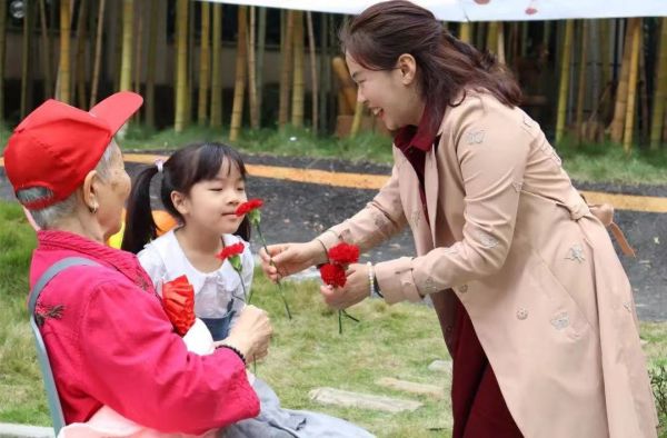 幼兒園小朋友和園長曾莉?yàn)槔先双I(xiàn)花。新絲路幼兒園供圖