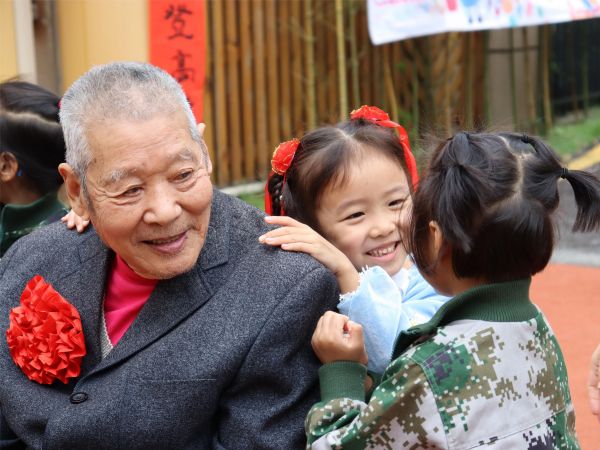 兩位孩子正在為爺爺捶背。新絲路幼兒園供圖