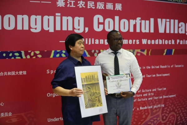 綦江農(nóng)民版畫院院長桂煥勇手持楊榮作品《開放中的重慶》與坦桑尼亞國家博物館執(zhí)行館長合影。重慶文藝職院供圖